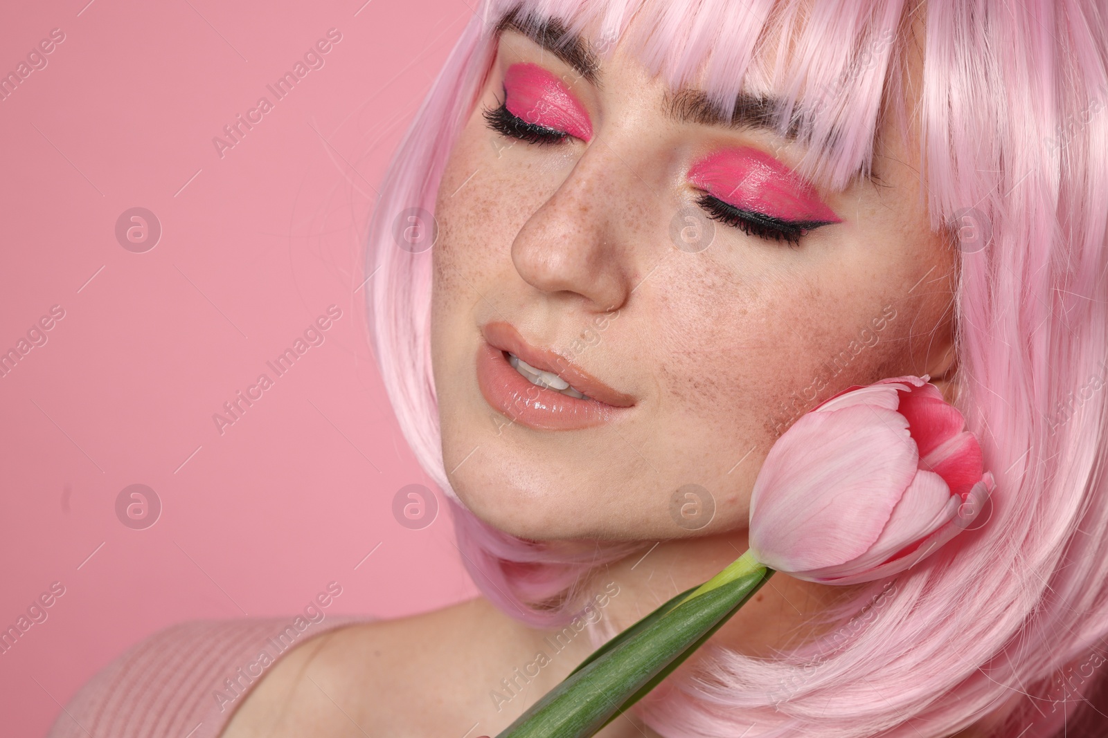 Photo of Beautiful woman with bright makeup, fake freckles and tulip on pink background, closeup