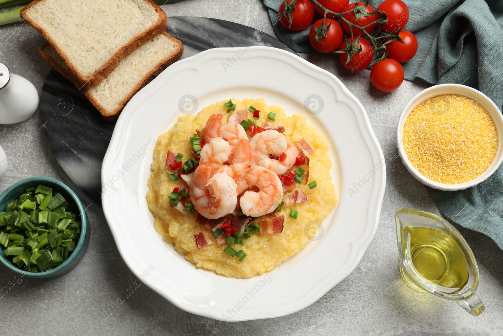 Photo of Plate with fresh tasty shrimps, bacon, grits, green onion and pepper on gray textured table, flat lay