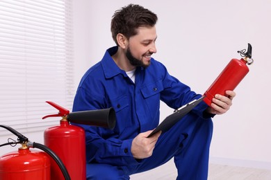 Man with clipboard checking fire extinguisher indoors