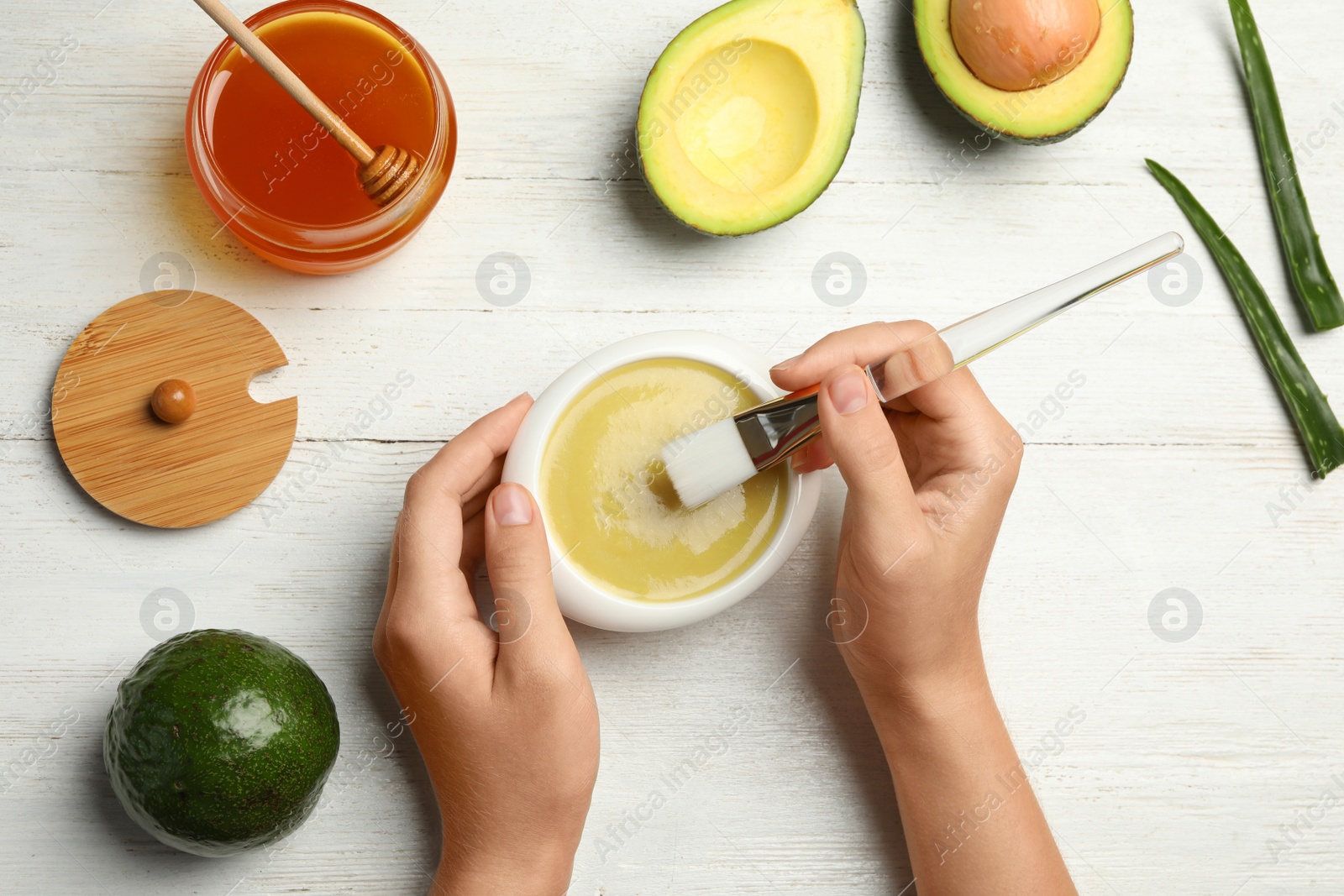 Photo of Woman with handmade face mask, brush and ingredients at white wooden table, top view