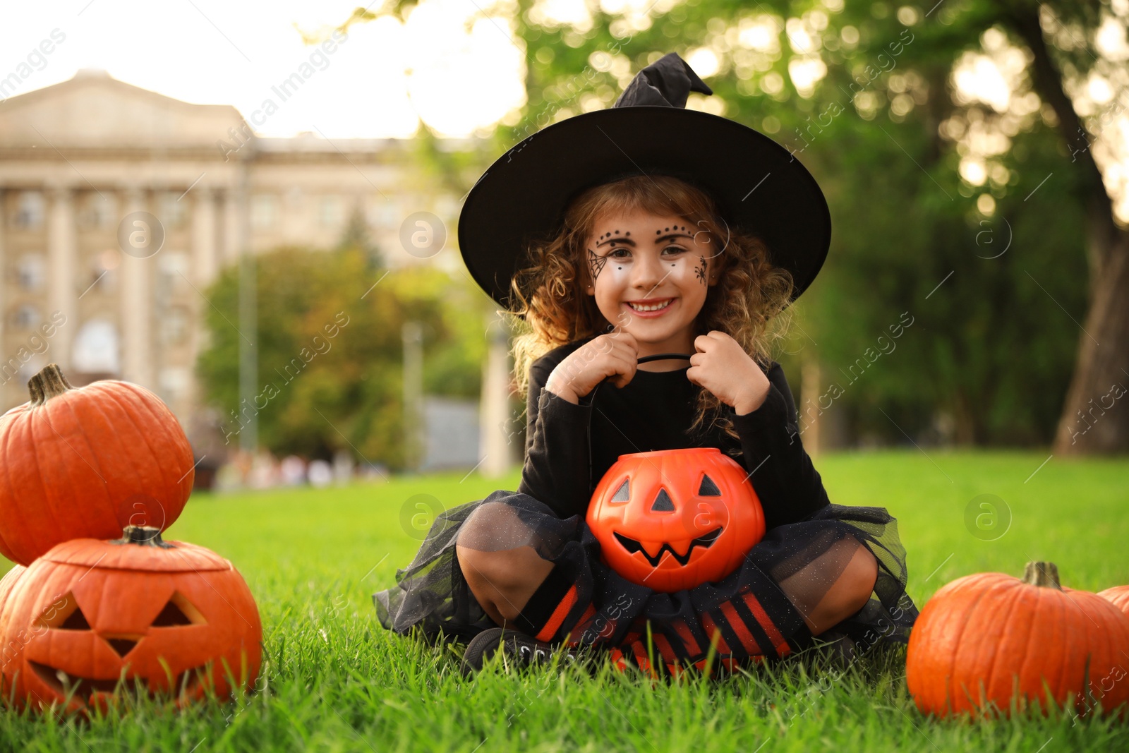 Photo of Cute little girl with pumpkin candy bucket wearing Halloween costume in park