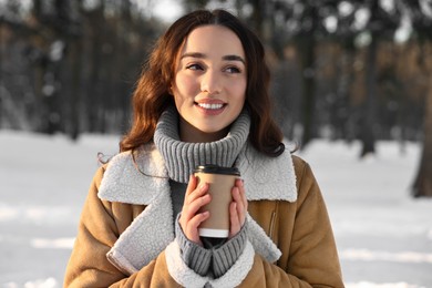 Portrait of smiling woman with paper cup of coffee in snowy park