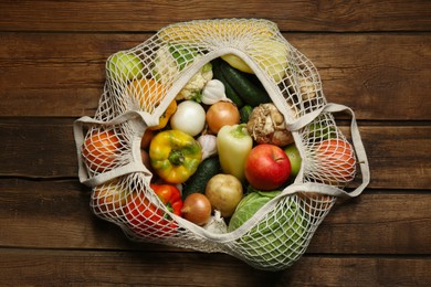 Photo of Different fresh vegetables in net bag on wooden table, top view. Farmer harvesting