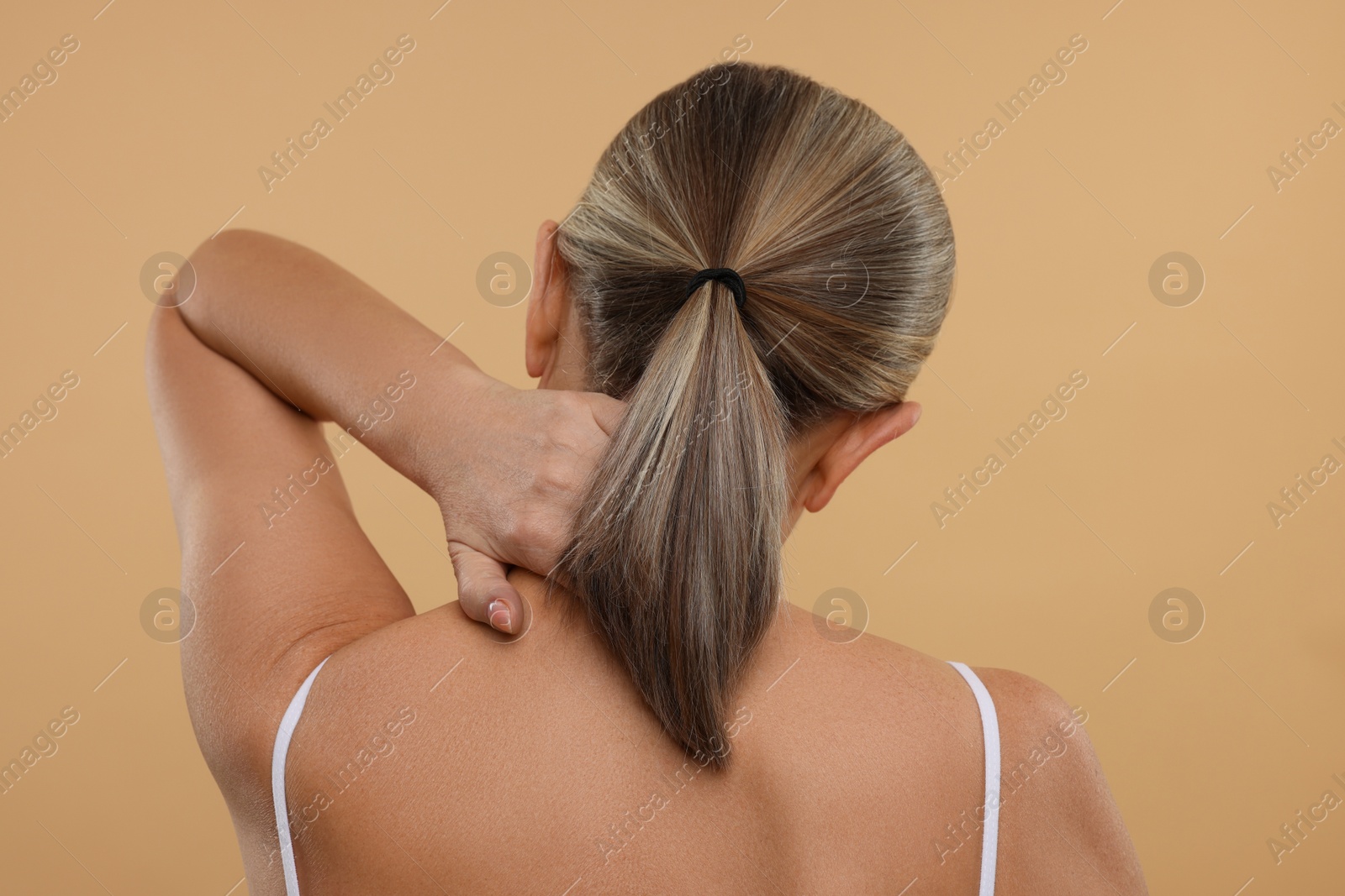 Photo of Mature woman suffering from pain in her neck on beige background, back view