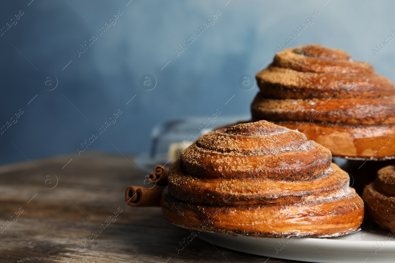 Photo of Plate with baked cinnamon rolls on wooden table, closeup. Space for text