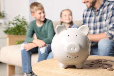 Photo of Happy family at home, focus on piggy bank. Space for text