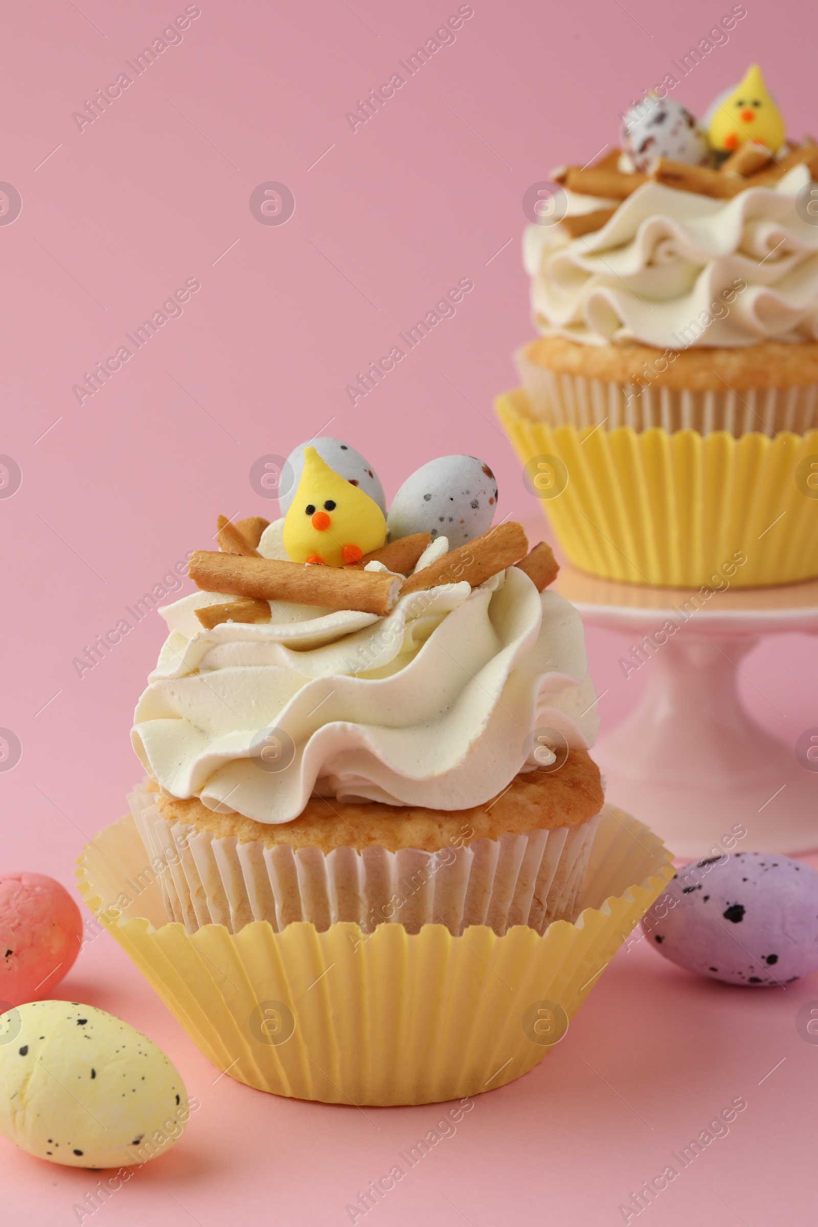 Photo of Tasty Easter cupcakes with vanilla cream and candies on pink background