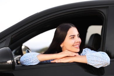 Photo of Enjoying trip. Portrait of beautiful happy woman in car, view from outside