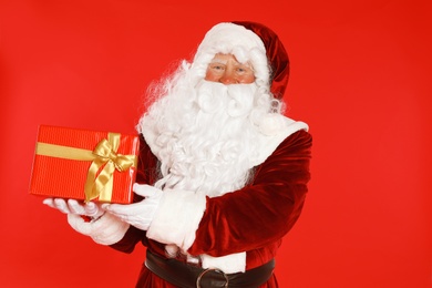 Photo of Authentic Santa Claus with gift box on red background