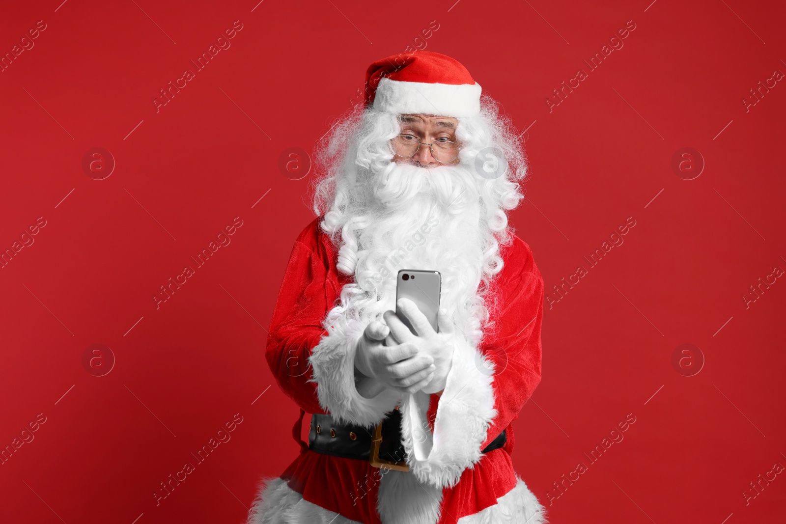 Photo of Merry Christmas. Santa Claus using smartphone on red background