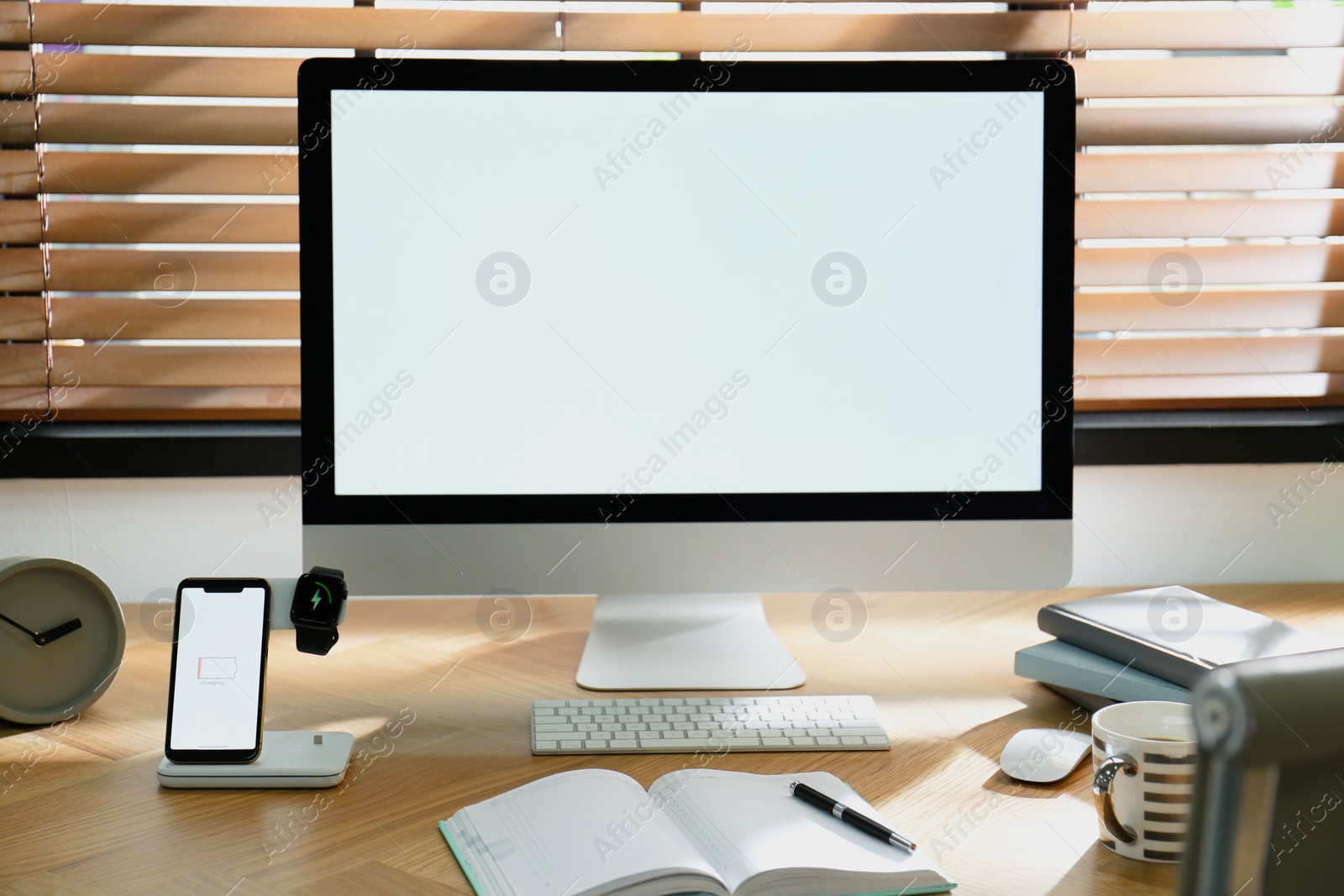 Photo of Modern workplace with smartphone and watch charging on wireless pad