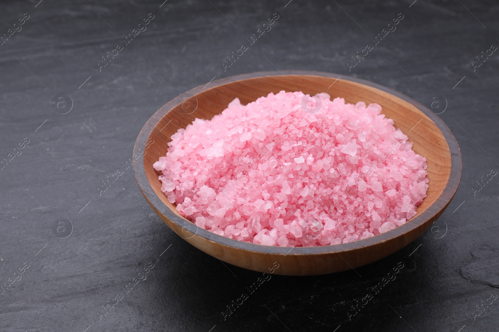 Photo of Bowl with pink sea salt on black table, closeup