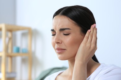 Young woman suffering from ear pain at home