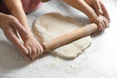 Father and child rolling raw dough at white table, closeup