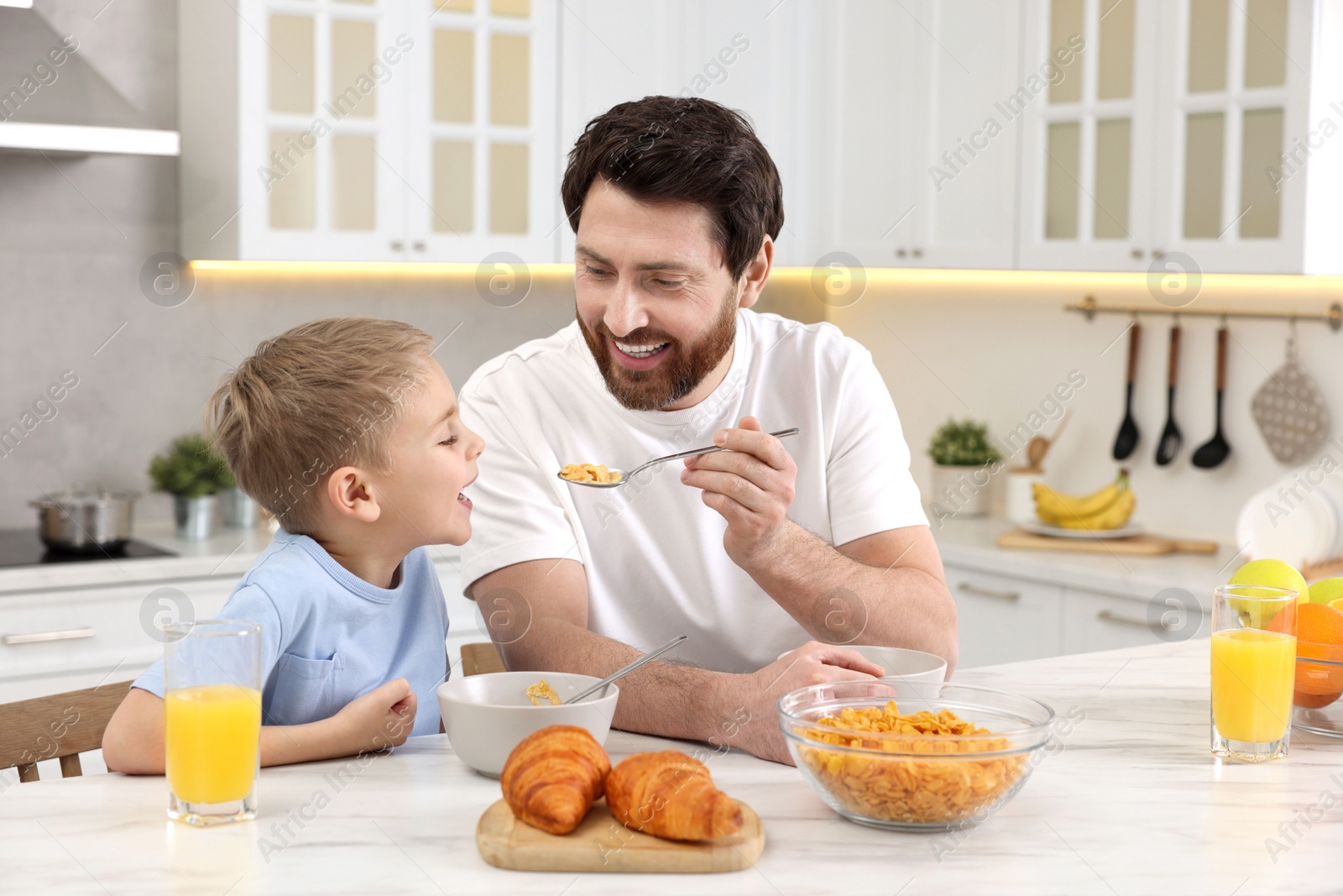 Photo of Father and his cute little son having breakfast at table in kitchen