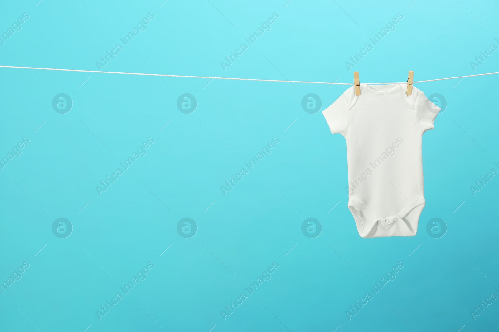 Photo of White baby onesie hanging on clothes line against blue background, space for text. Laundry day