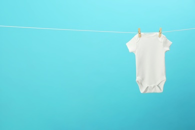 White baby onesie hanging on clothes line against blue background, space for text. Laundry day