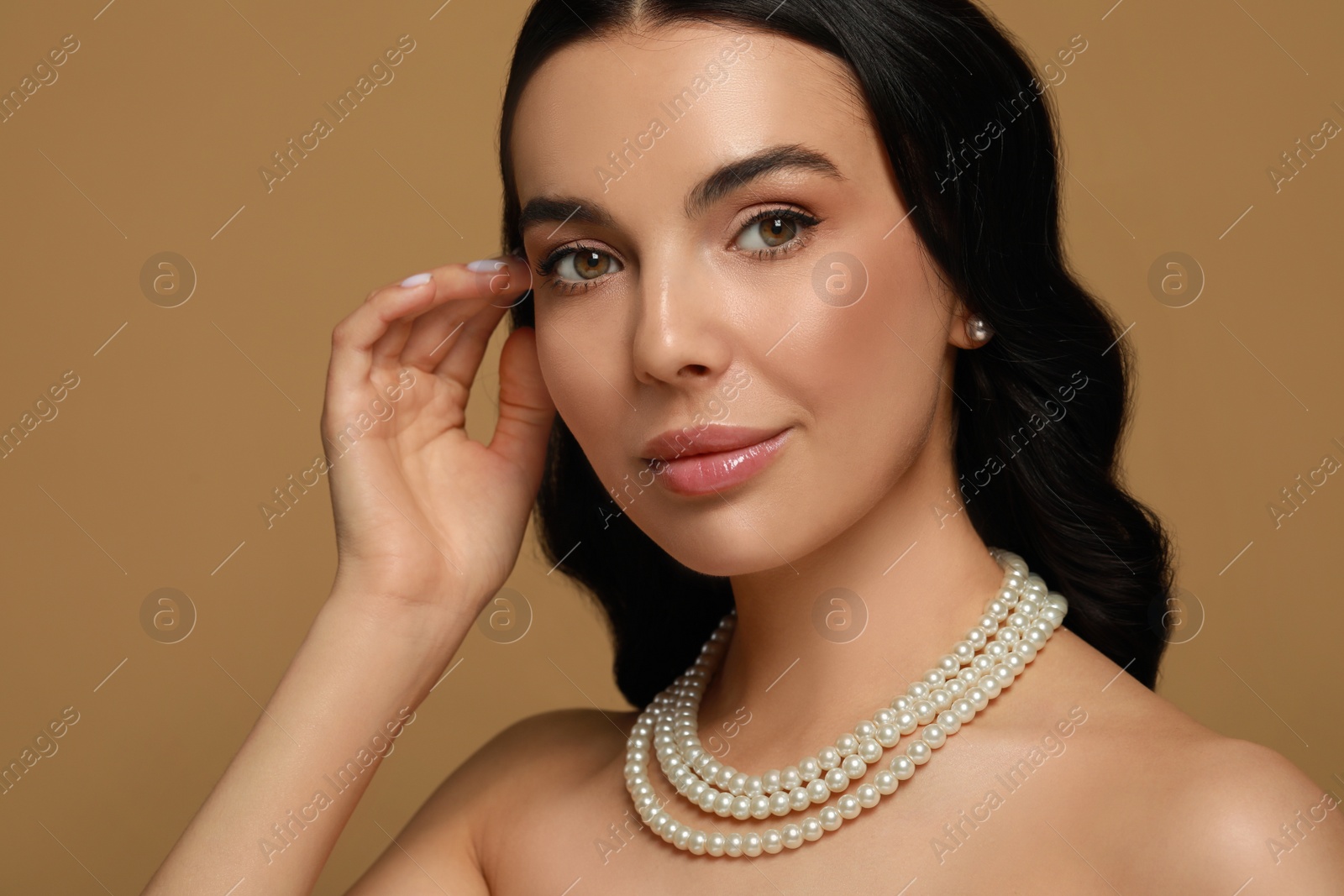 Photo of Young woman wearing elegant pearl jewelry on brown background