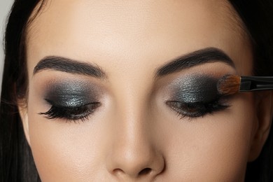 Photo of Applying dark eye shadow with brush onto woman's face, closeup. Beautiful evening makeup