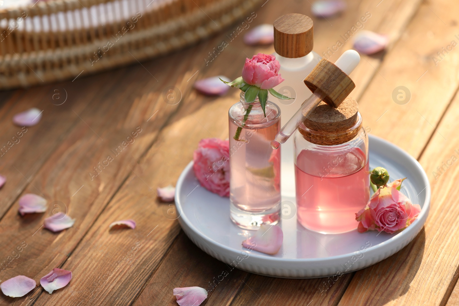 Photo of Bottles of rose essential oil and flowers on wooden table, space for text