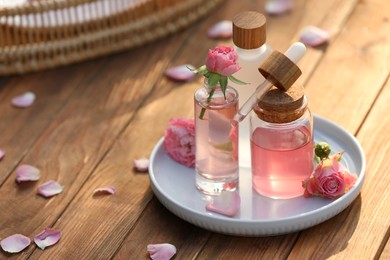 Photo of Bottles of rose essential oil and flowers on wooden table, space for text
