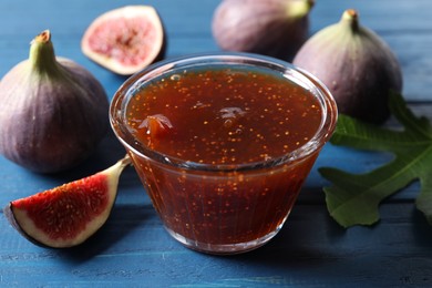 Glass bowl with tasty sweet jam and fresh figs on blue wooden table, closeup