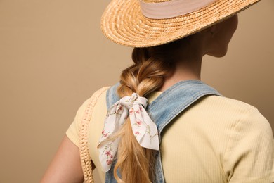 Young woman with hat and stylish bandana on beige background, closeup