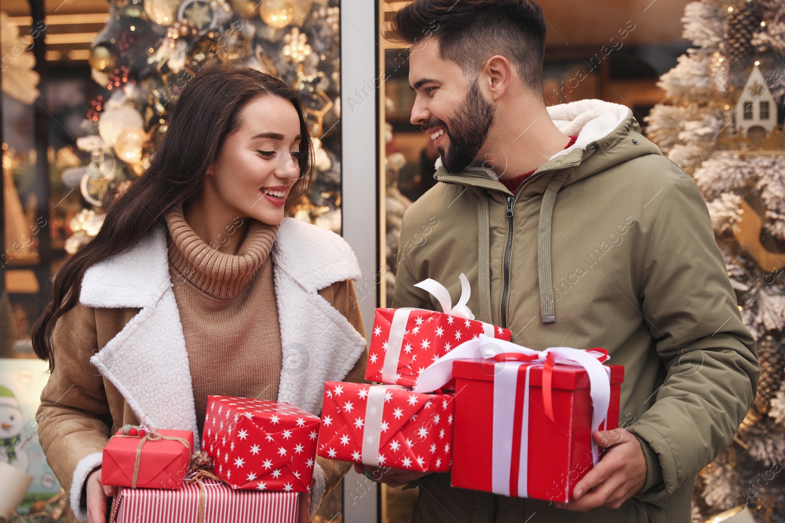 Photo of Lovely couple with presents near store decorated for Christmas outdoors