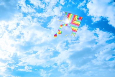 Bright striped rainbow kite flying in blue sky on sunny day