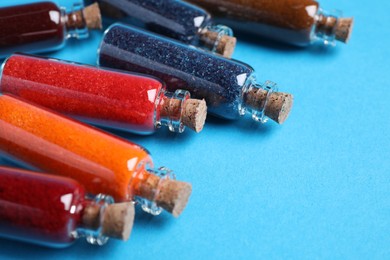 Glass bottles with different food coloring on light blue background, closeup. Space for text