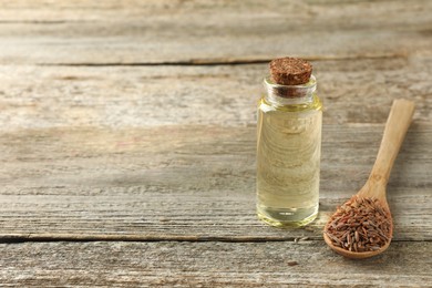 Spoon of caraway (Persian cumin) seeds and essential oil on wooden table, space for text