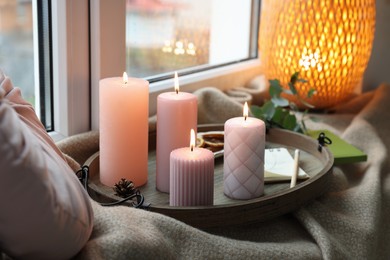 Photo of Tray with burning wax candles and decor on window sill indoors