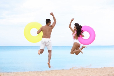 Photo of Happy young couple having fun with inflatable rings on beach near sea
