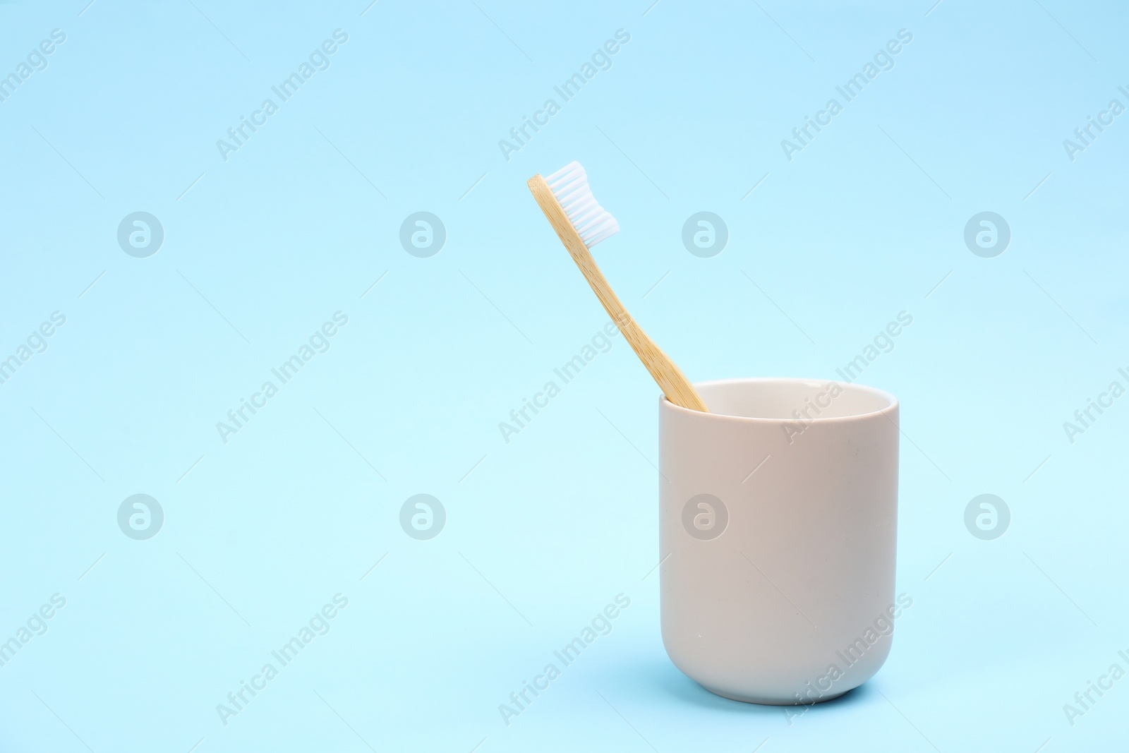 Photo of Toothbrush made of bamboo in holder on light blue background. Space for text