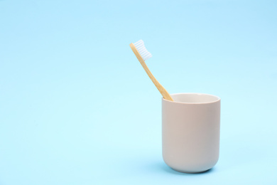 Photo of Toothbrush made of bamboo in holder on light blue background. Space for text