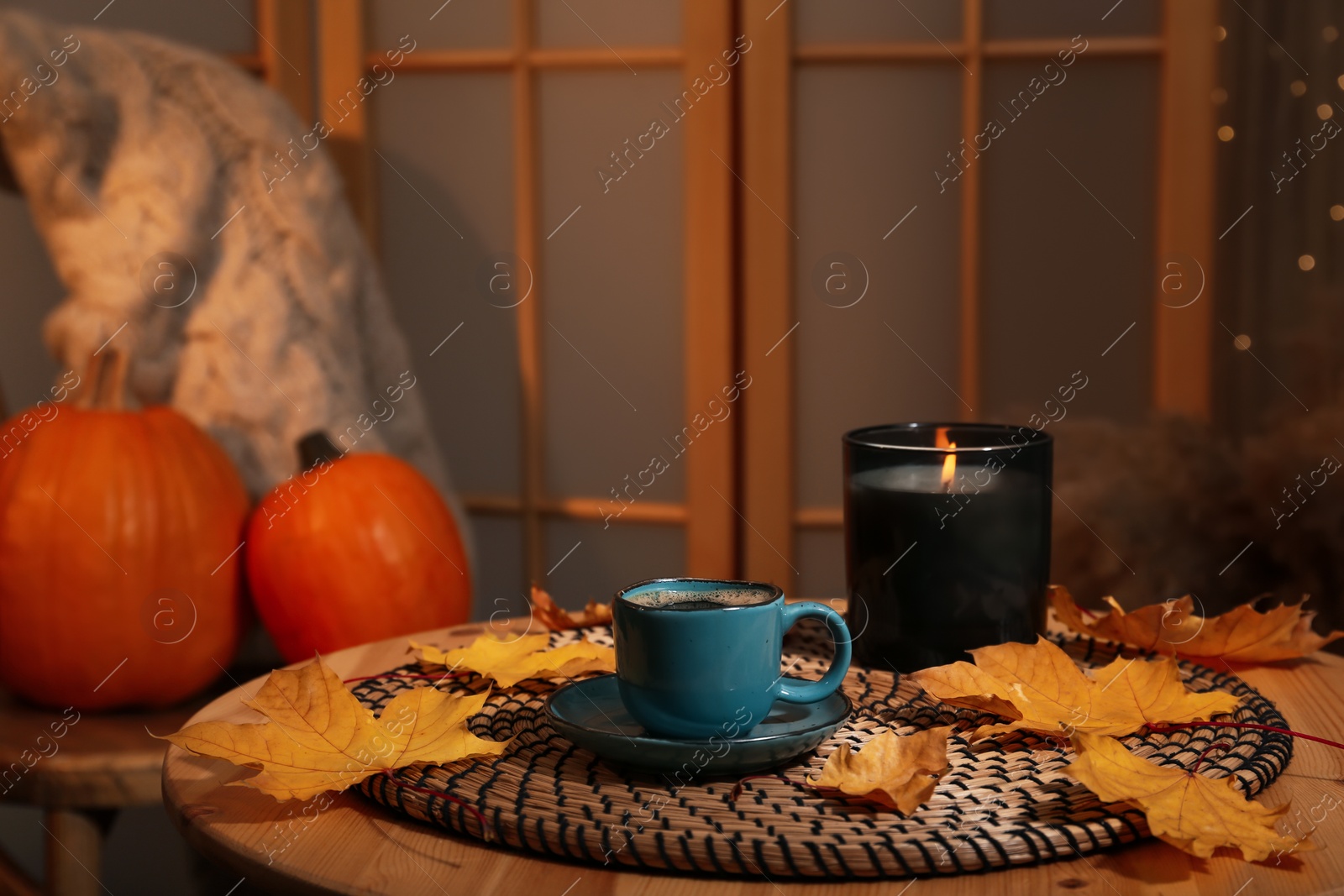 Photo of Cup of aromatic coffee, candle and autumn leaves on wooden table indoors, space for text