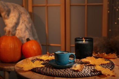 Cup of aromatic coffee, candle and autumn leaves on wooden table indoors, space for text