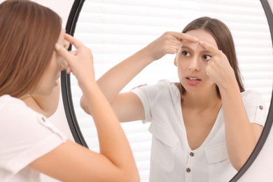 Woman with skin problem looking at mirror indoors