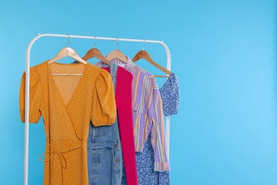 Photo of Rack with stylish women`s clothes on wooden hangers against light blue background, space for text