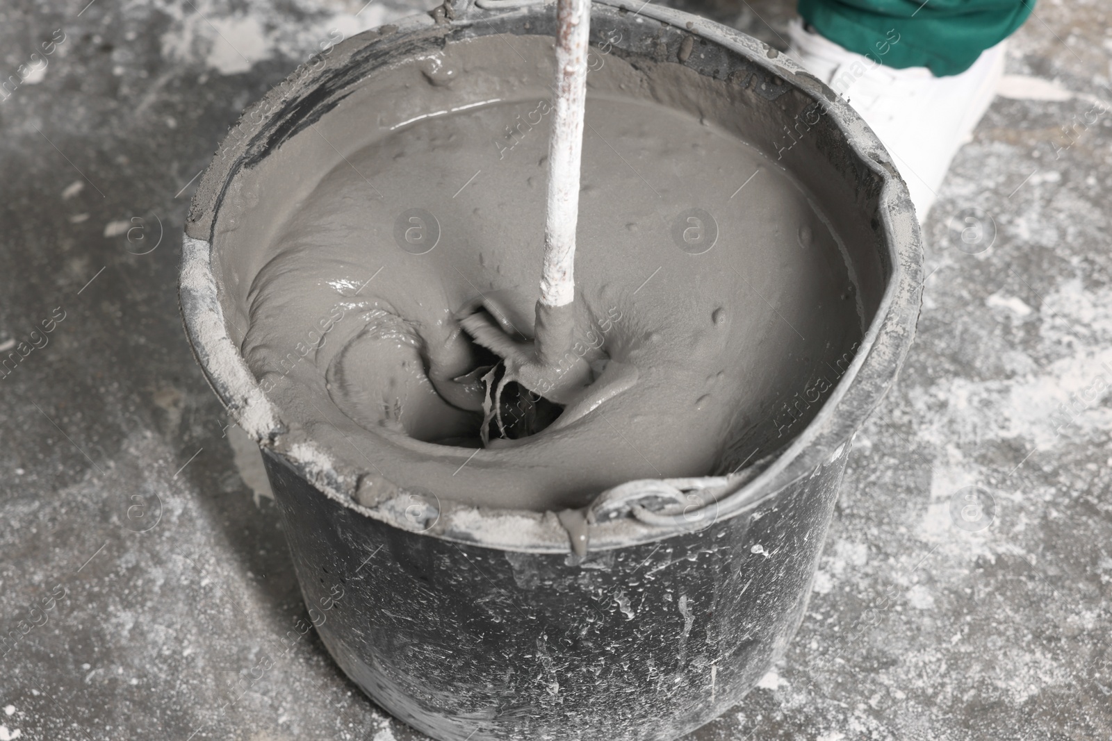 Photo of Worker mixing concrete in bucket indoors, closeup