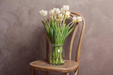 Photo of Vase with beautiful tulips on chair, indoors