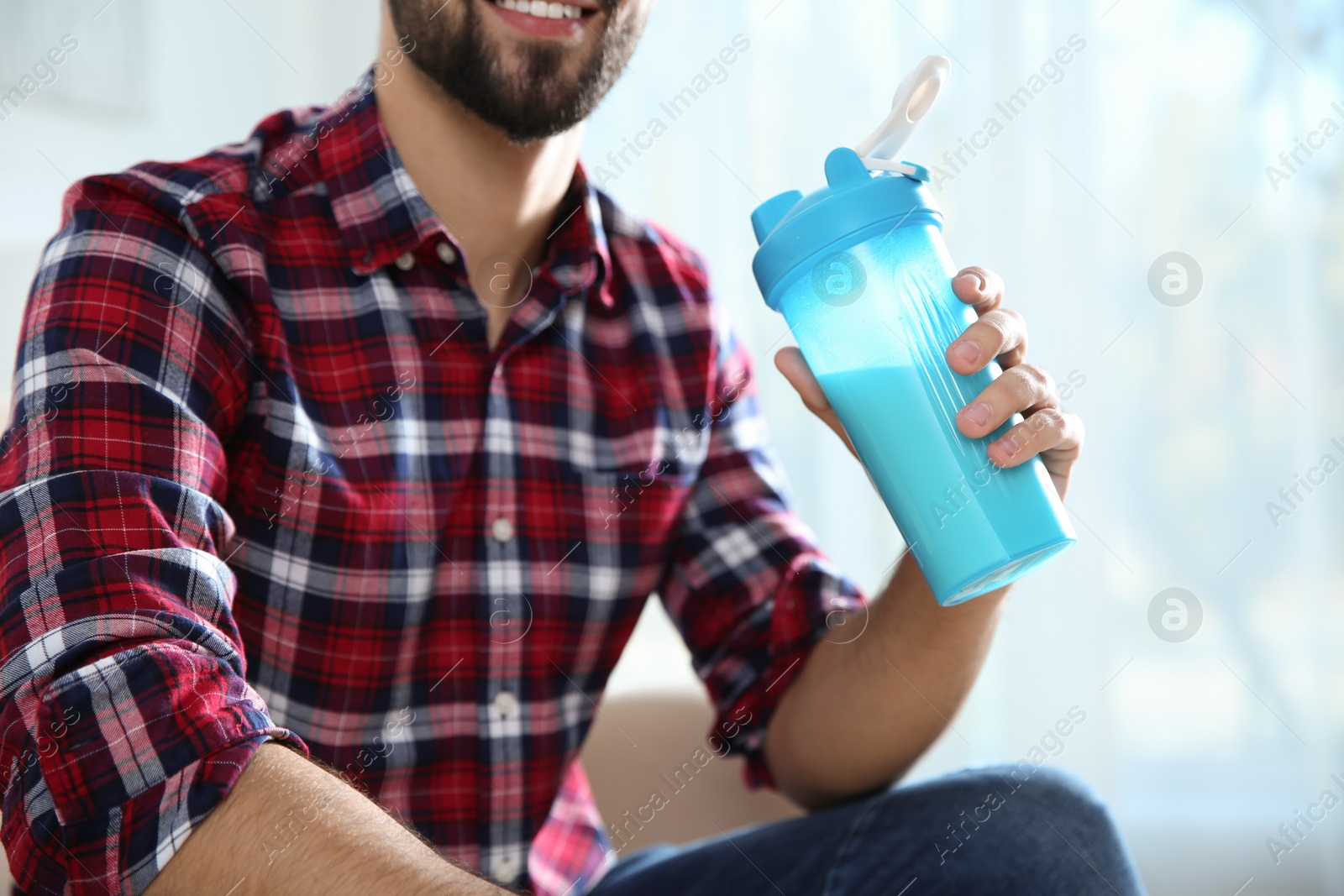 Photo of Young man with bottle of protein shake at home, closeup