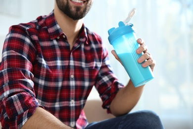 Photo of Young man with bottle of protein shake at home, closeup