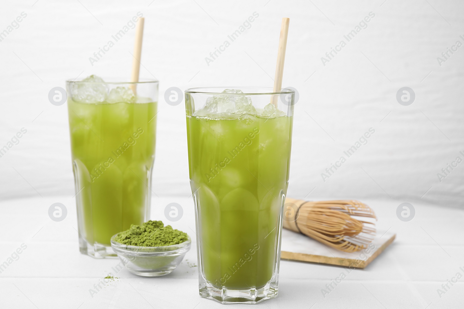 Photo of Delicious iced green matcha tea, powder and bamboo whisk on white table