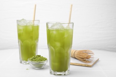 Delicious iced green matcha tea, powder and bamboo whisk on white table