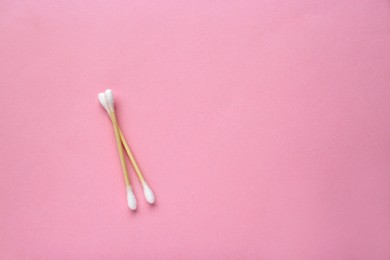 Photo of Two wooden cotton buds on pink background, flat lay. Space for text