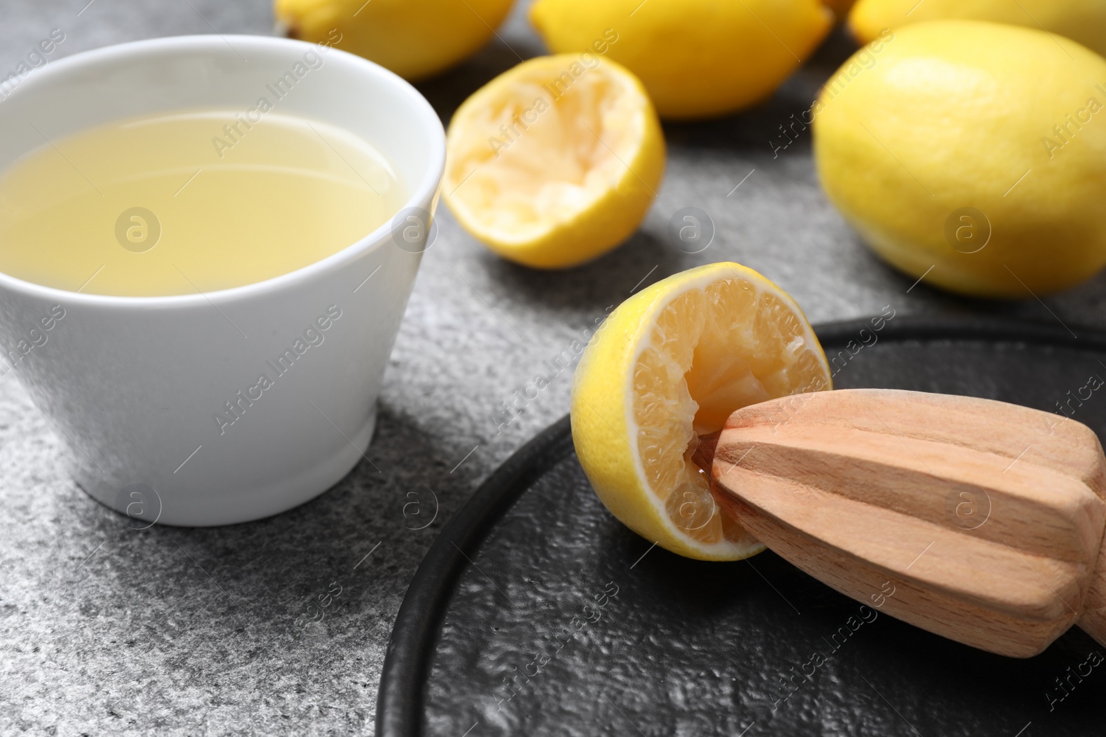 Photo of Freshly squeezed lemon juice and reamer on grey table, closeup