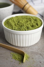 Photo of Green matcha powder and bamboo scoop on light grey table, closeup