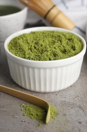 Green matcha powder and bamboo scoop on light grey table, closeup