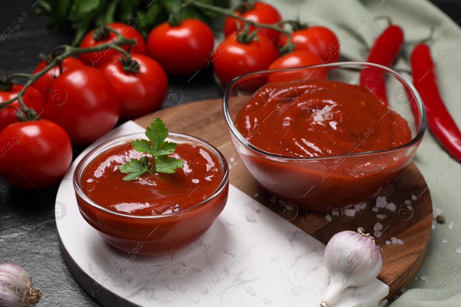 Photo of Organic ketchup in bowls and ingredients on black table. Tomato sauce